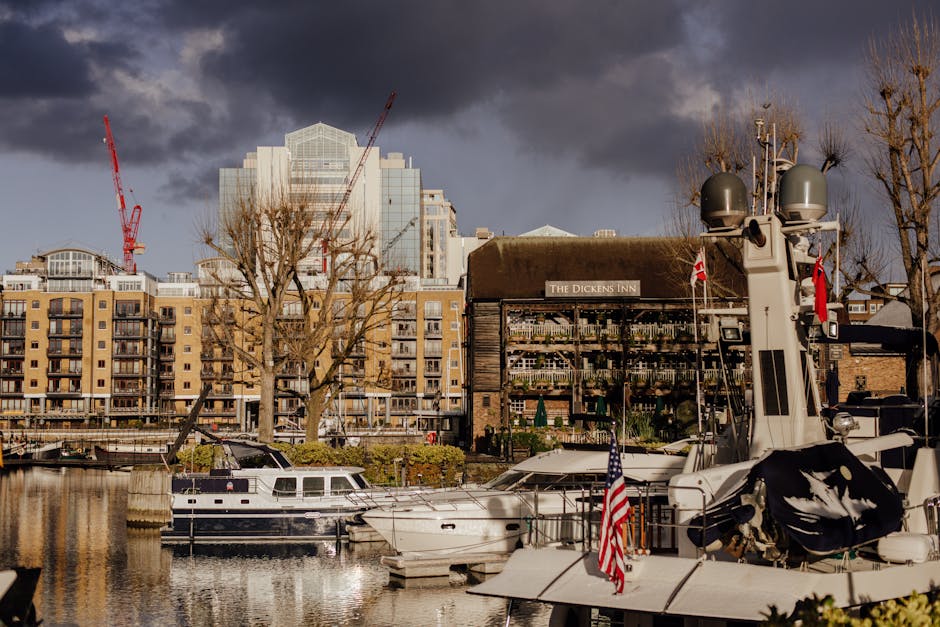 A busy outdoor scene in front of a large, multi-story wooden building called 'The Dickens Inn' with a sign on the roof, featuring exposed timber framing and decorated with flower boxes on each level.